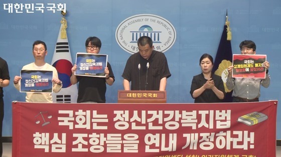 국회는 정신건강복지법, 핵심 조항들을 연내 개정하라! 현수막을 들고있음21일 서울 여의도 국회소통관에서 개최된 기자회견에서 발언하는 한국정신장애인연합회 신설철 상임대표. ⓒ국회방송 